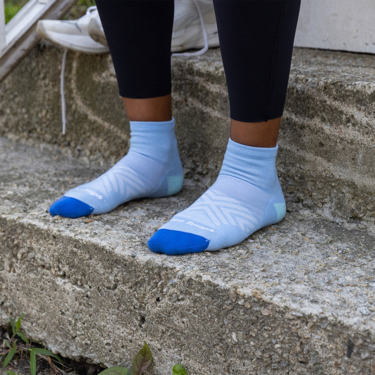 Runner wearing Darn Tough women's Run Quarter socks in Sky with running shoes on outdoor steps