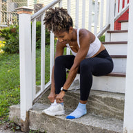 Woman tying her running shoe on steps while wearing Darn Tough Run Quarter socks in Sky
