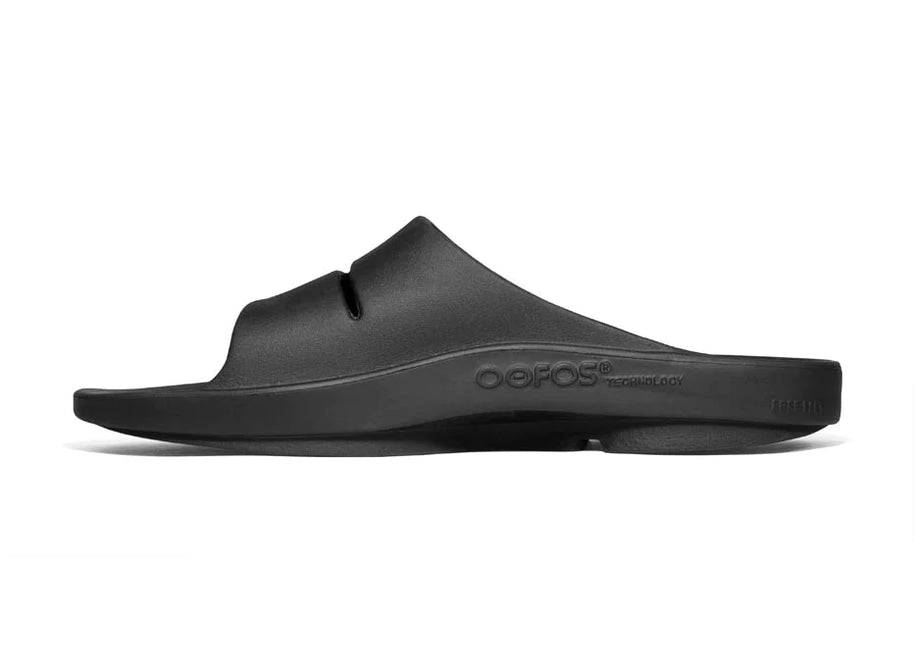 OOahh - Unisex in black by Oofos, lightweight slides with agile OOfoam strap and patented footbed for impact absorption and support.