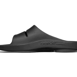 OOahh - Unisex in black by Oofos, lightweight slides with agile OOfoam strap and patented footbed for impact absorption and support.