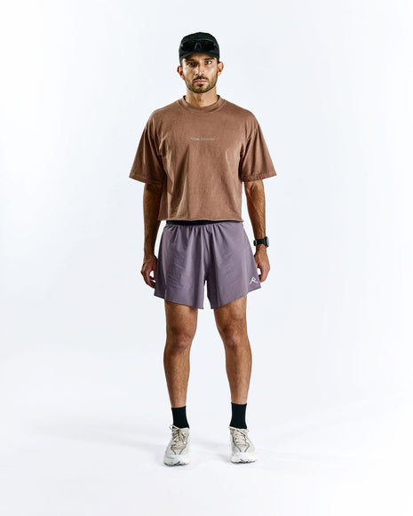 Model in a cap wearing Raide Research Trail Tech Short men's shorts in Dusk with a brown tee, front view