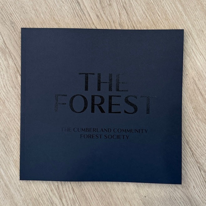 25 Years of the Cumberland Community Forest Society book in dark blue, featuring curated photos and evocative forest stories by local authors.