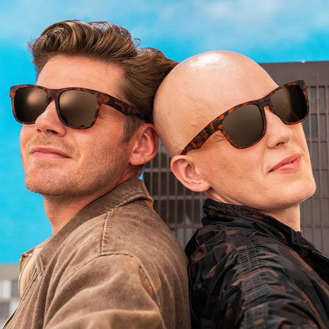 Two people standing back to back in a city wearing Goodr Hellhound Hallucinations tortoiseshell sunglasses