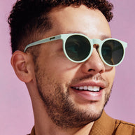 Smiling man against a pink background wearing Goodr Incognito Plant Parent sage green round sunglasses