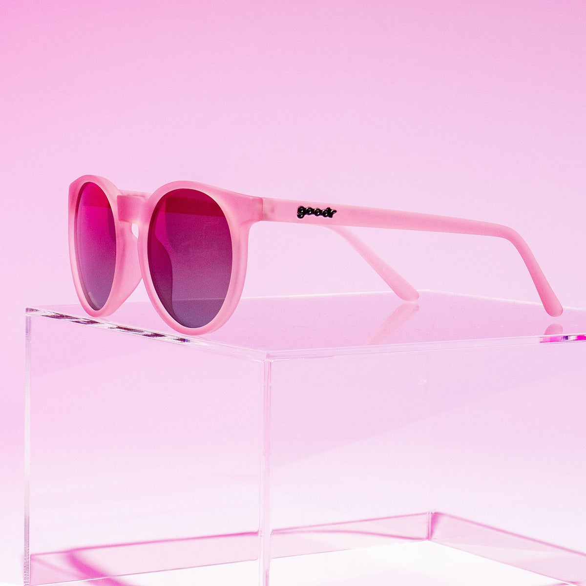 Goodr Mauve Mood Board sunglasses resting on a clear acrylic block against a pink backdrop