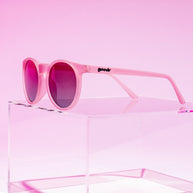 Goodr Mauve Mood Board sunglasses resting on a clear acrylic block against a pink backdrop