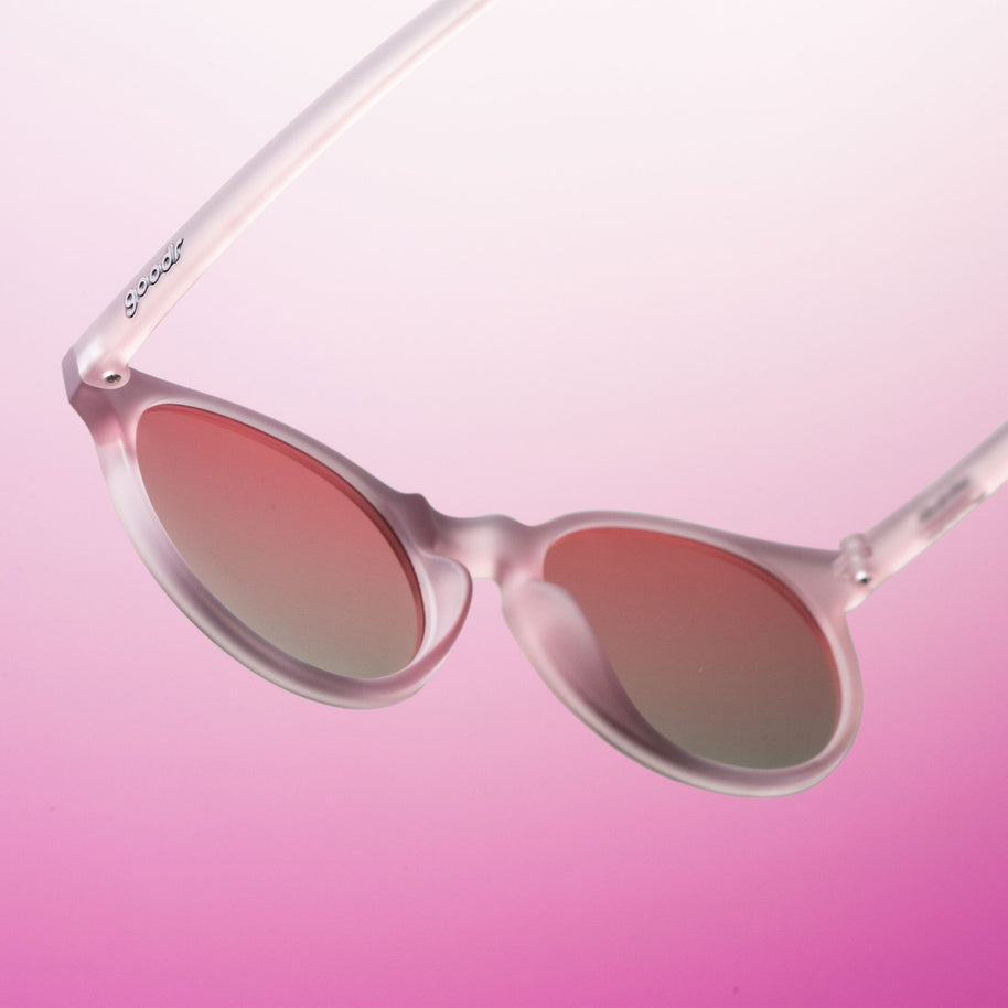 Close-up of the Goodr Mauve Mood Board sunglasses floating at an angle over a pink gradient background
