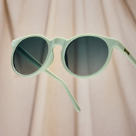 Close-up of the Goodr Incognito Plant Parent sunglasses with arms open against beige fabric
