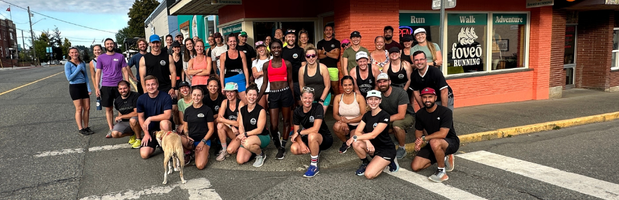 Group of diverse runners gathered outside a bright orange and green Foveo Running store on a sunny day in an urban setting