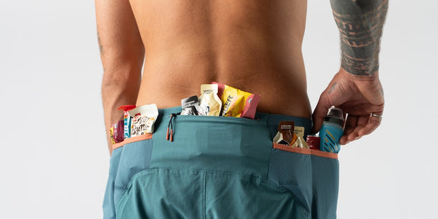 Close-up of male runner wearing teal running shorts with multiple energy gels and nutrition bars in rear pockets for long-distance running preparation