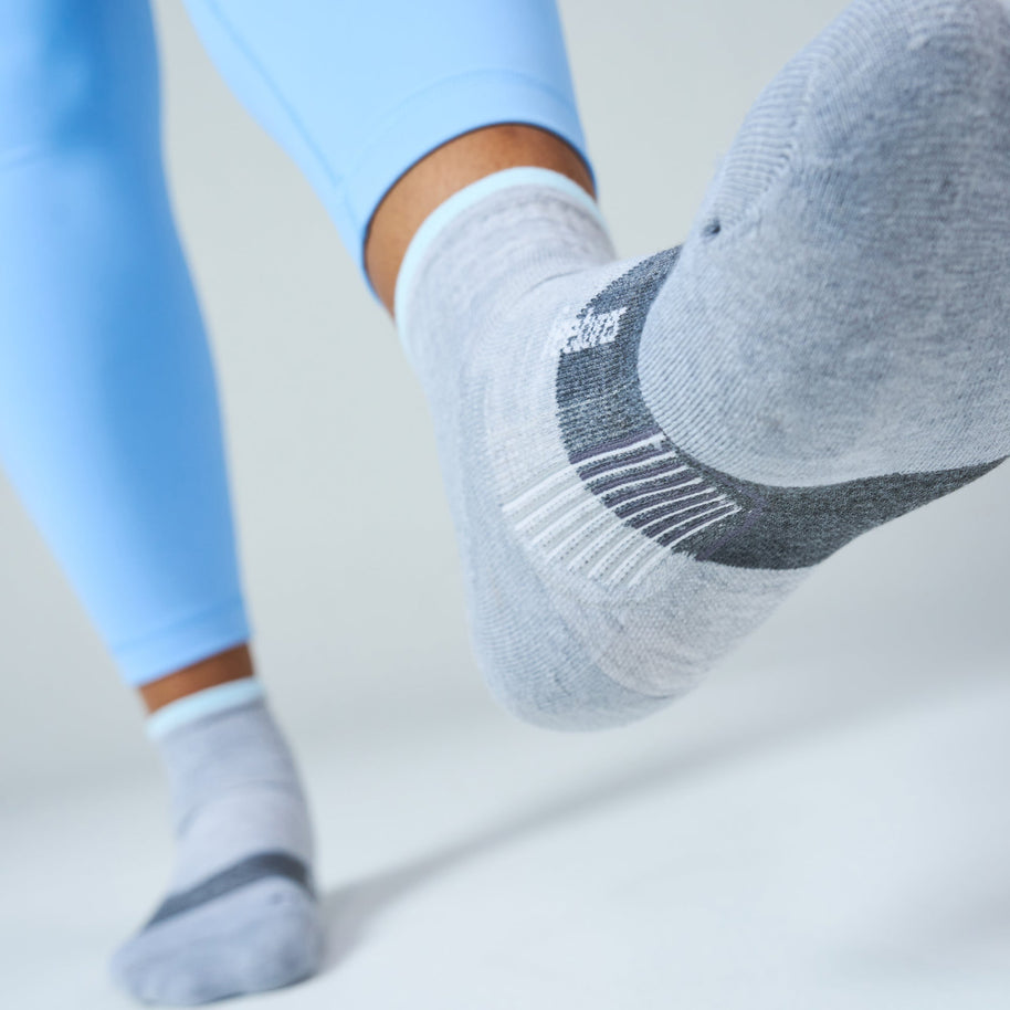 Runner in blue leggings stepping forward in Feetures Trail Max Cushion Quarter Socks in Light Grey
