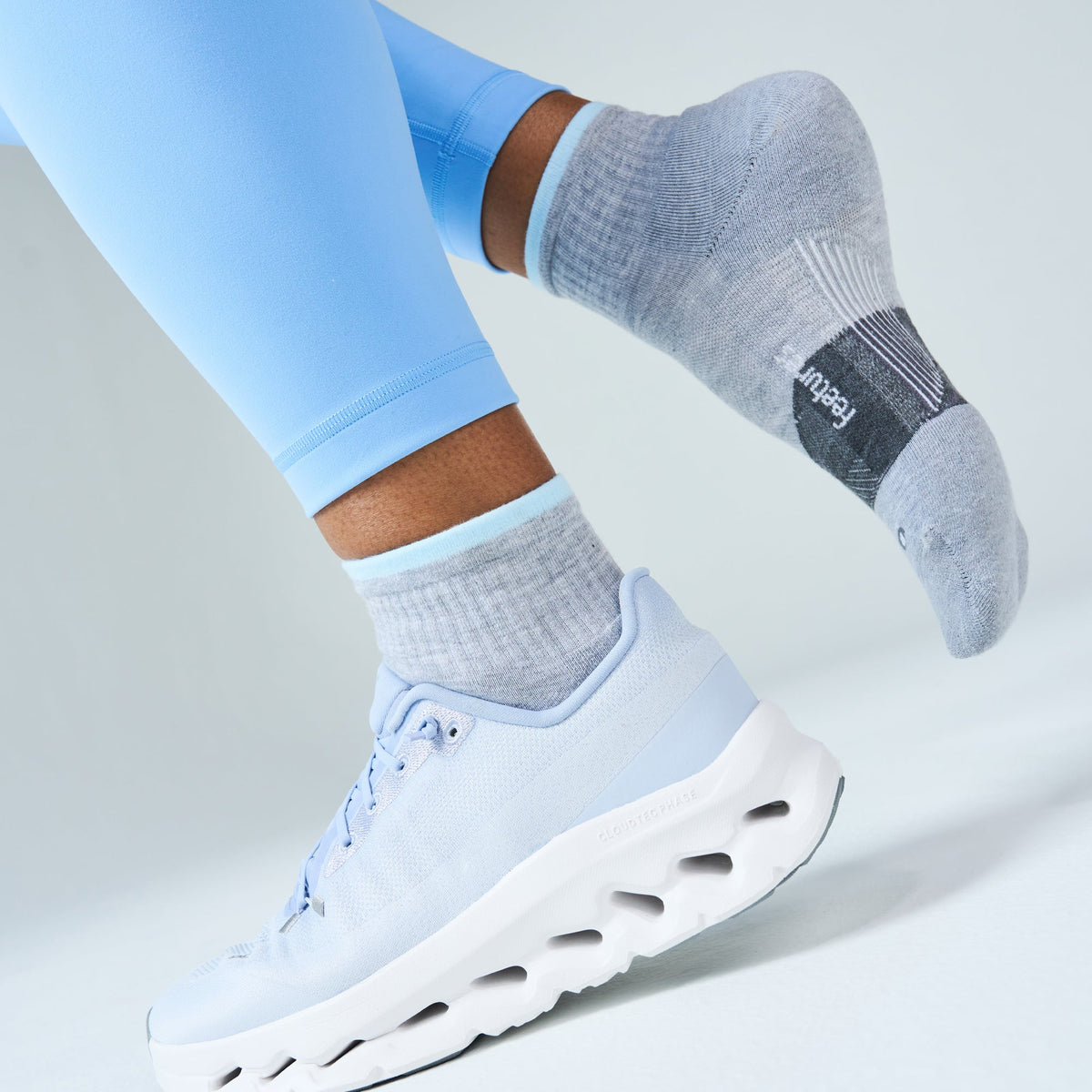 Runner in blue leggings and white shoes wearing Feetures Trail Max Cushion Quarter Socks in Light Grey