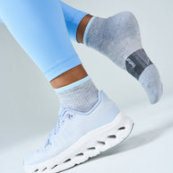 Runner in blue leggings and white shoes wearing Feetures Trail Max Cushion Quarter Socks in Light Grey