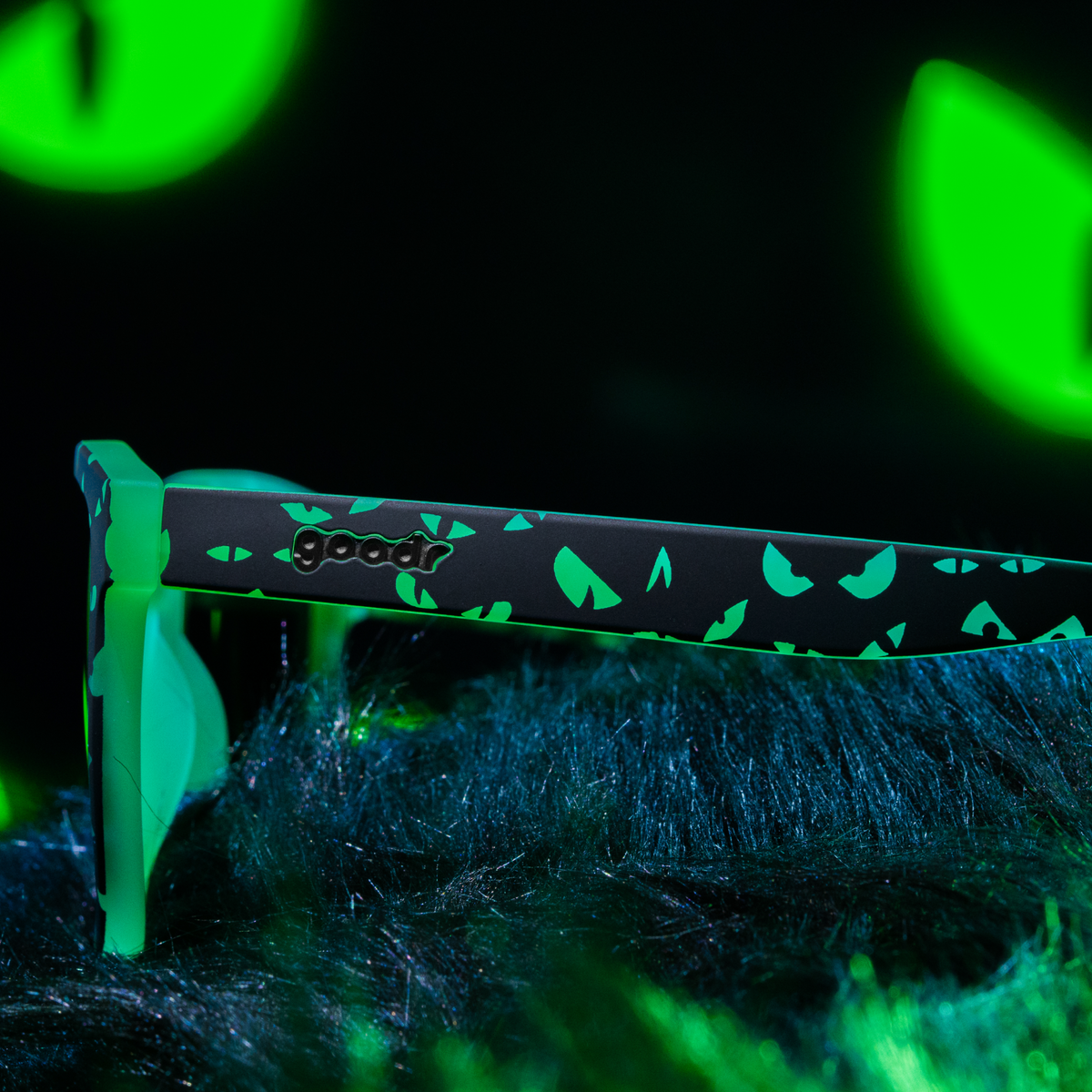 Close-up of the arm of the Goodr What Lurks In The Shadows sunglasses with green eye print and goodr logo