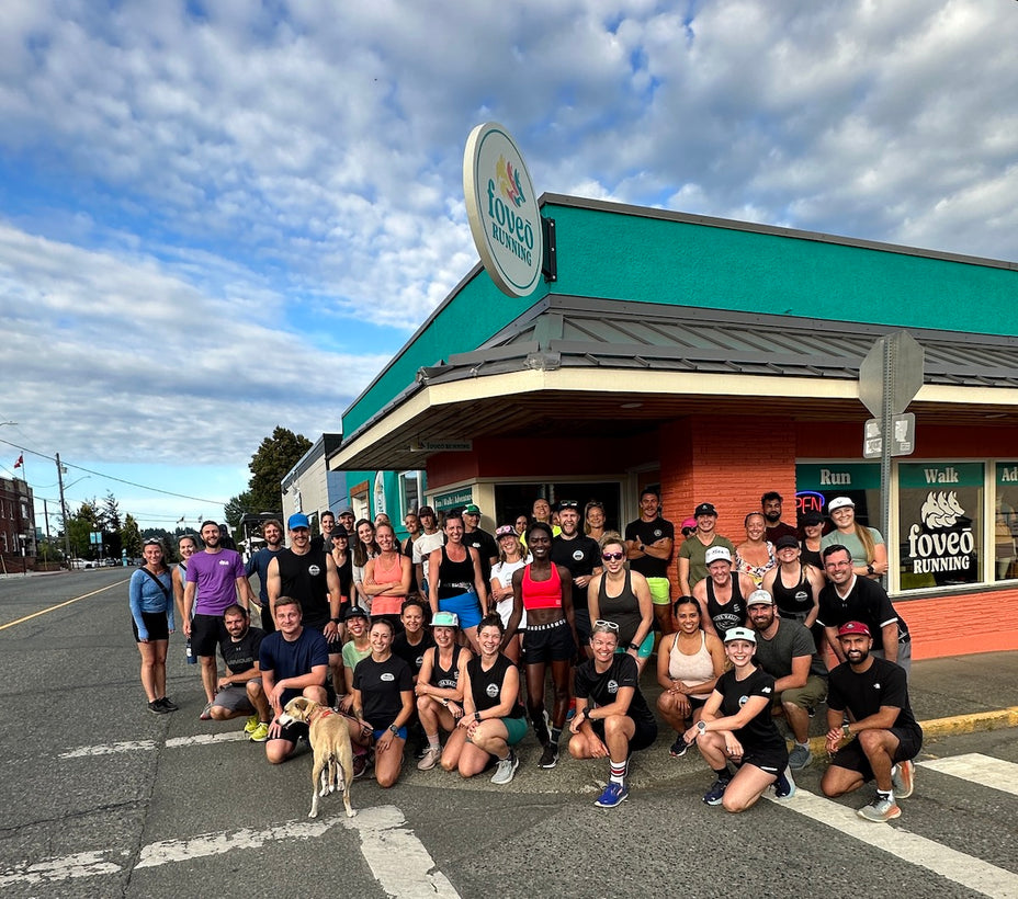 Group of diverse runners in athletic wear posing outside Loveo Running store on a cloudy day before a community run event