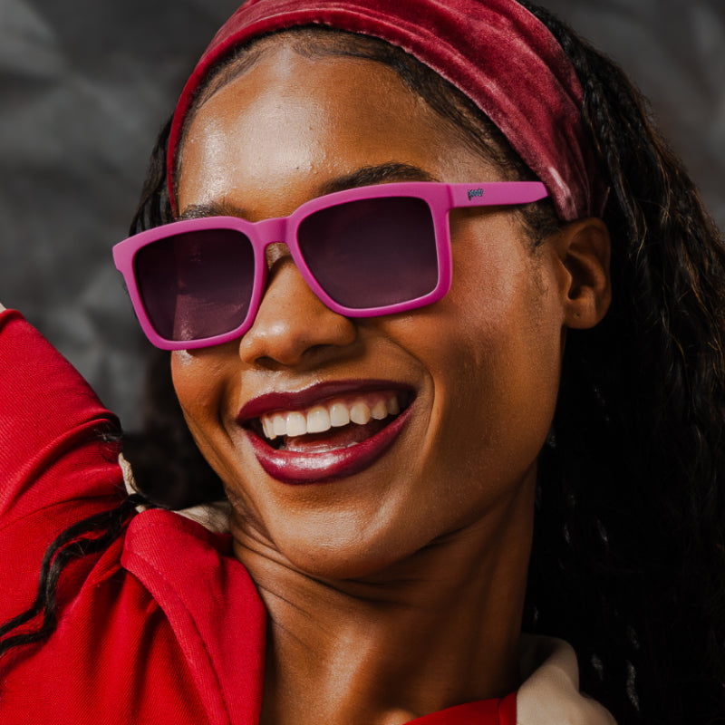 Laughing woman in a red headband and jacket wearing Goodr Living Highlight Reel magenta sunglasses