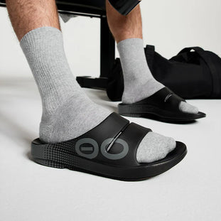 OOahh Sport - Unisex by Oofos in black with bold hand-painted strap, OOfoam cushioning for comfort, ideal for post-running recovery
