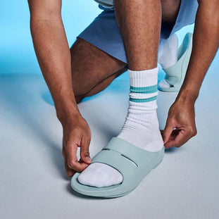 OOahh - Unisex by Oofos in light blue, lightweight slides with OOfoam strap for impact absorption and all-day comfort