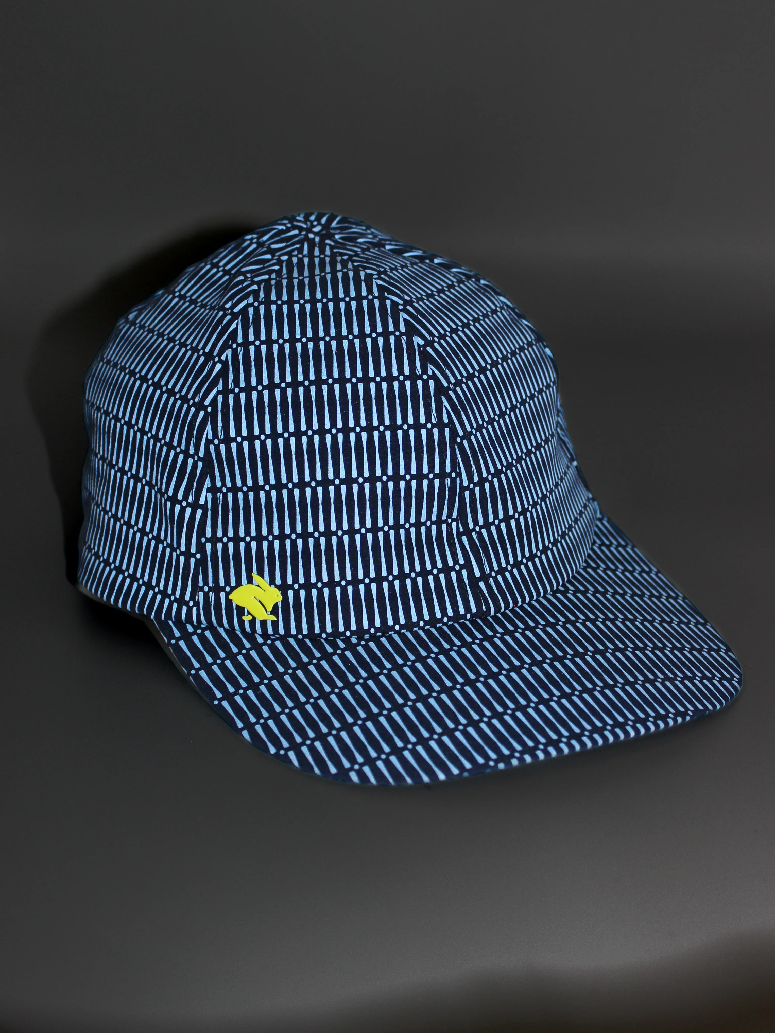 Low Light Tech Cap by Rabbit in blue with reflective pattern and yellow logo, designed for visibility in low light conditions