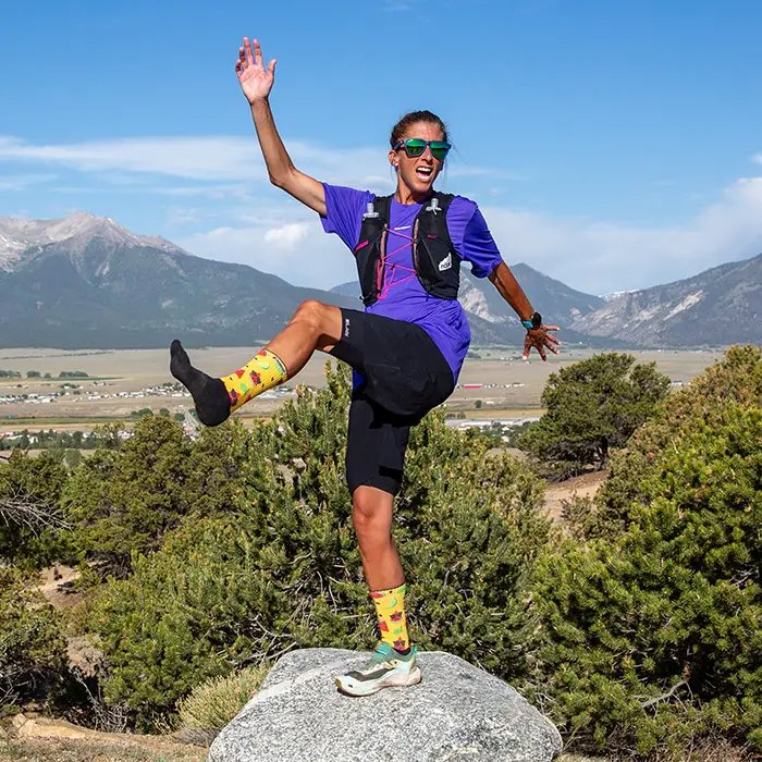Woman posing on a rock with one leg raised, wearing yellow watermelon Injinji The Courtney Crew socks in Solar Slice