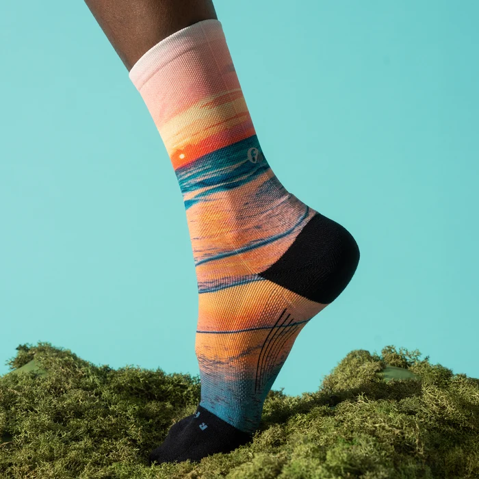 Foot stepping on moss wearing a Feetures Elite Light Cushion Mini Crew sock in Sunset Glow on a teal backdrop