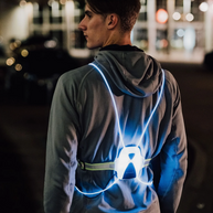Runner at night on a city street, back view wearing a NiteVest Rechargeable LED Safety Vest glowing blue over a grey hoodie