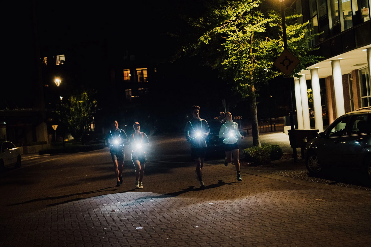 Group of runners on a city street at night with NiteVest Rechargeable LED Safety Vest chest lights shining