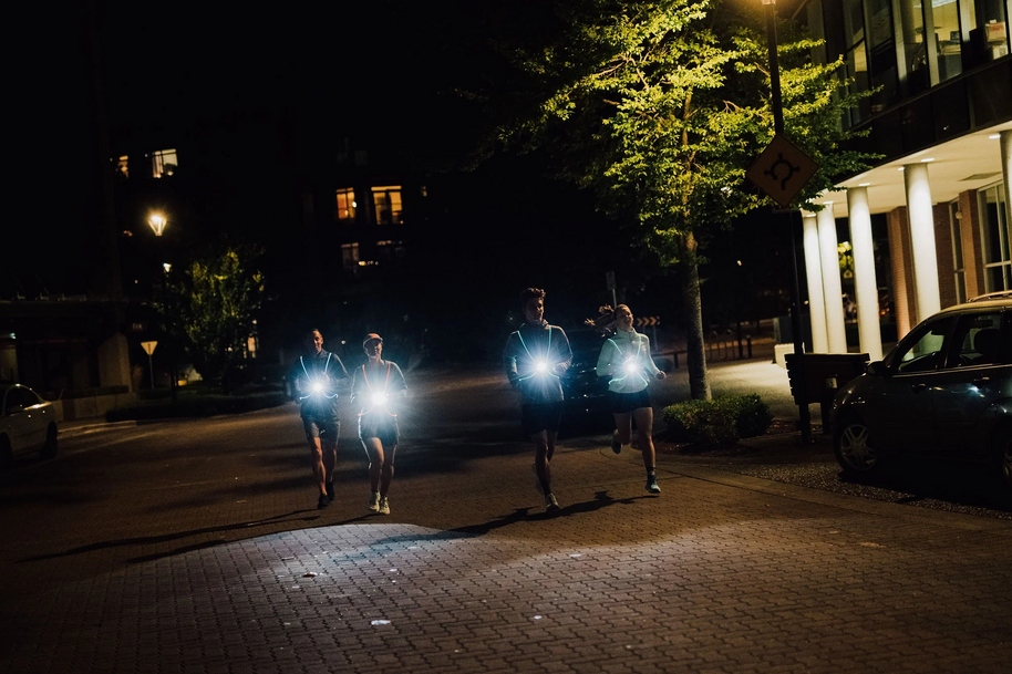 Group of runners on a city street at night with NiteVest Rechargeable LED Safety Vest chest lights shining