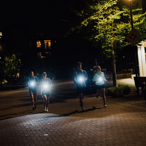 Group of runners on a city street at night with NiteVest Rechargeable LED Safety Vest chest lights shining