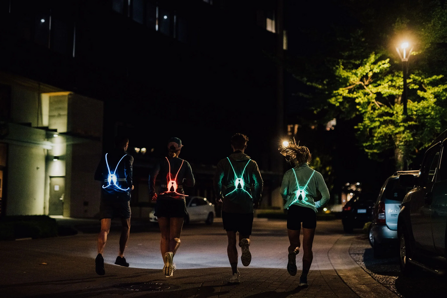 Four runners seen from behind on a night street wearing NiteVest Rechargeable LED Safety Vests glowing in different colours