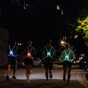 Four runners seen from behind on a night street wearing NiteVest Rechargeable LED Safety Vests glowing in different colours