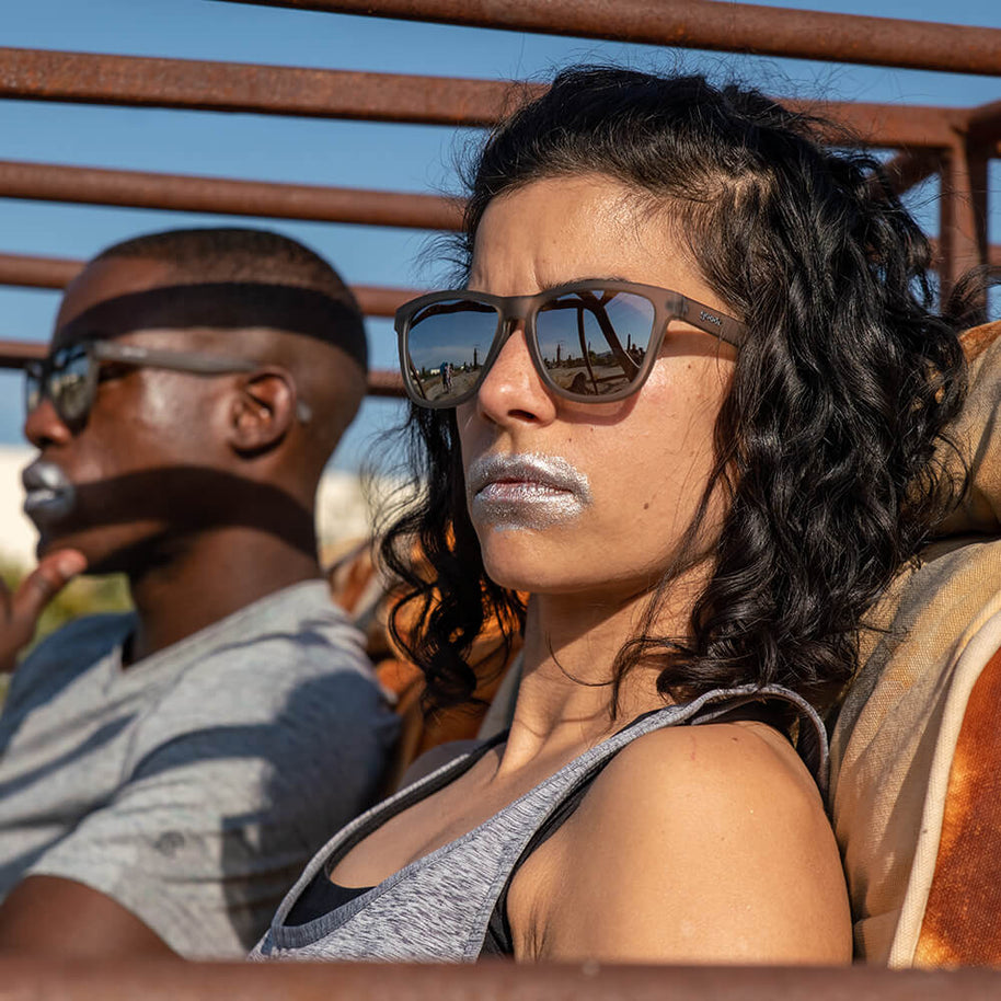 Woman with curly hair wearing Goodr Going to Valhalla... Witness! sunglasses, seated beside a man in a headband